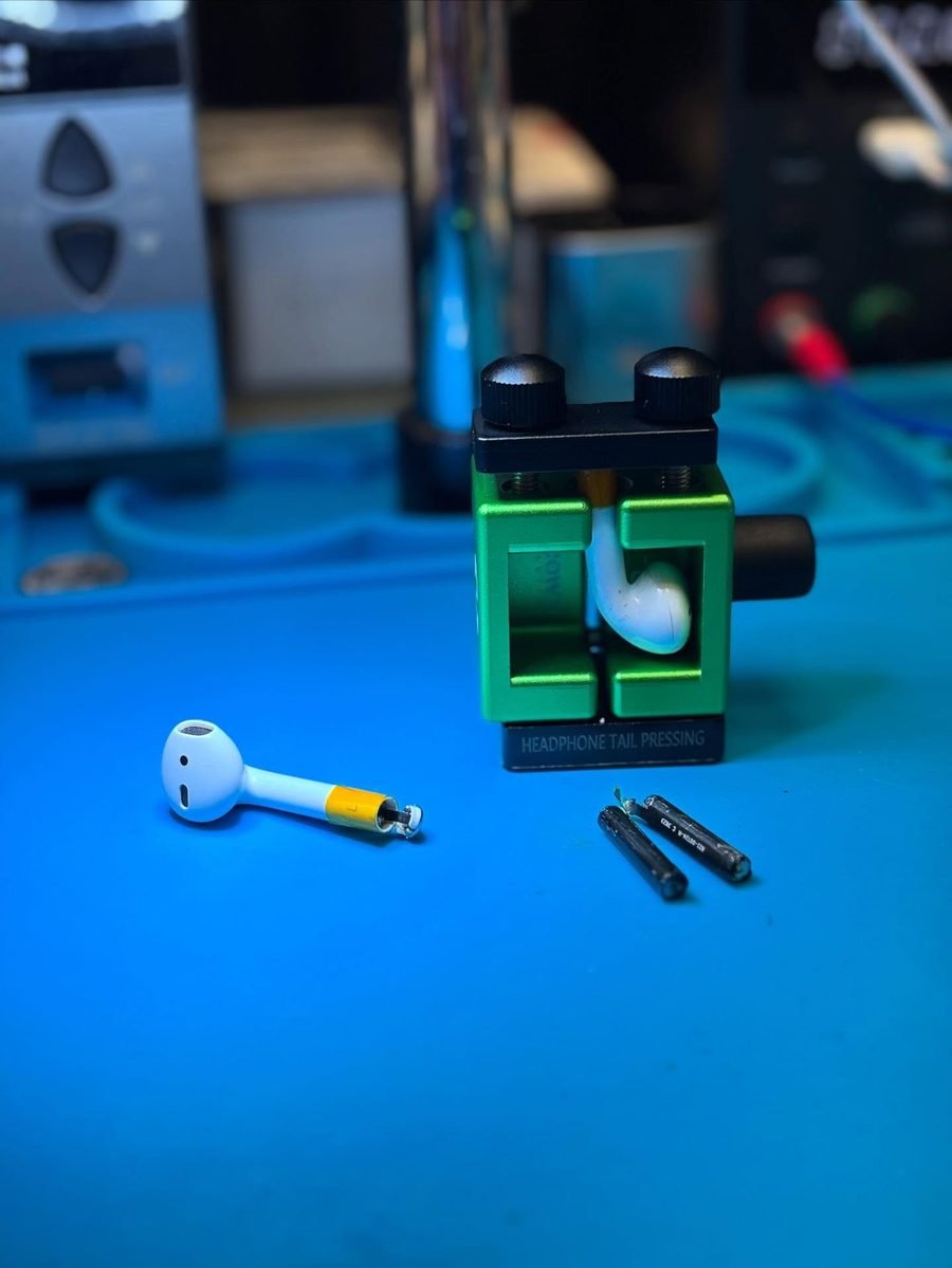 AirPod con la batería del tallo reemplazada, junto a la prensa de trabajo
